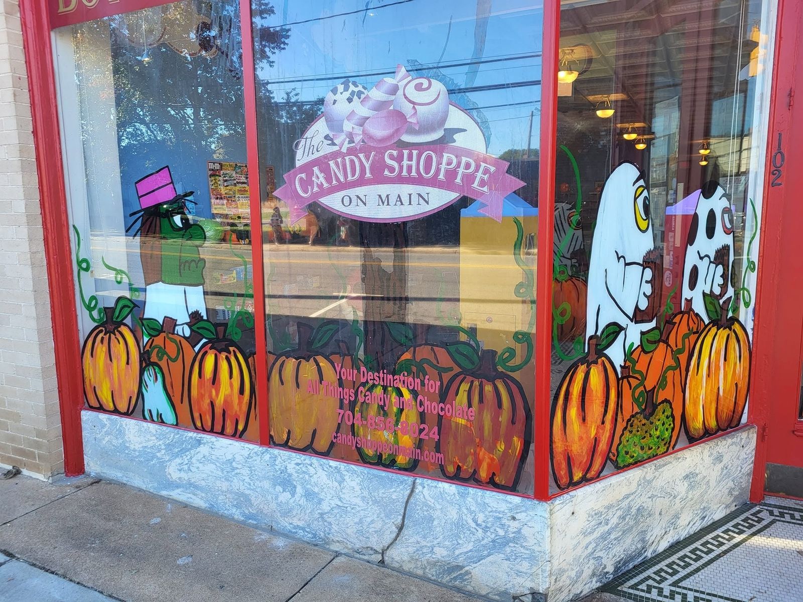 Painted corner window with the shop logo and autumn pumpkins at The Candy Shoppe on Main