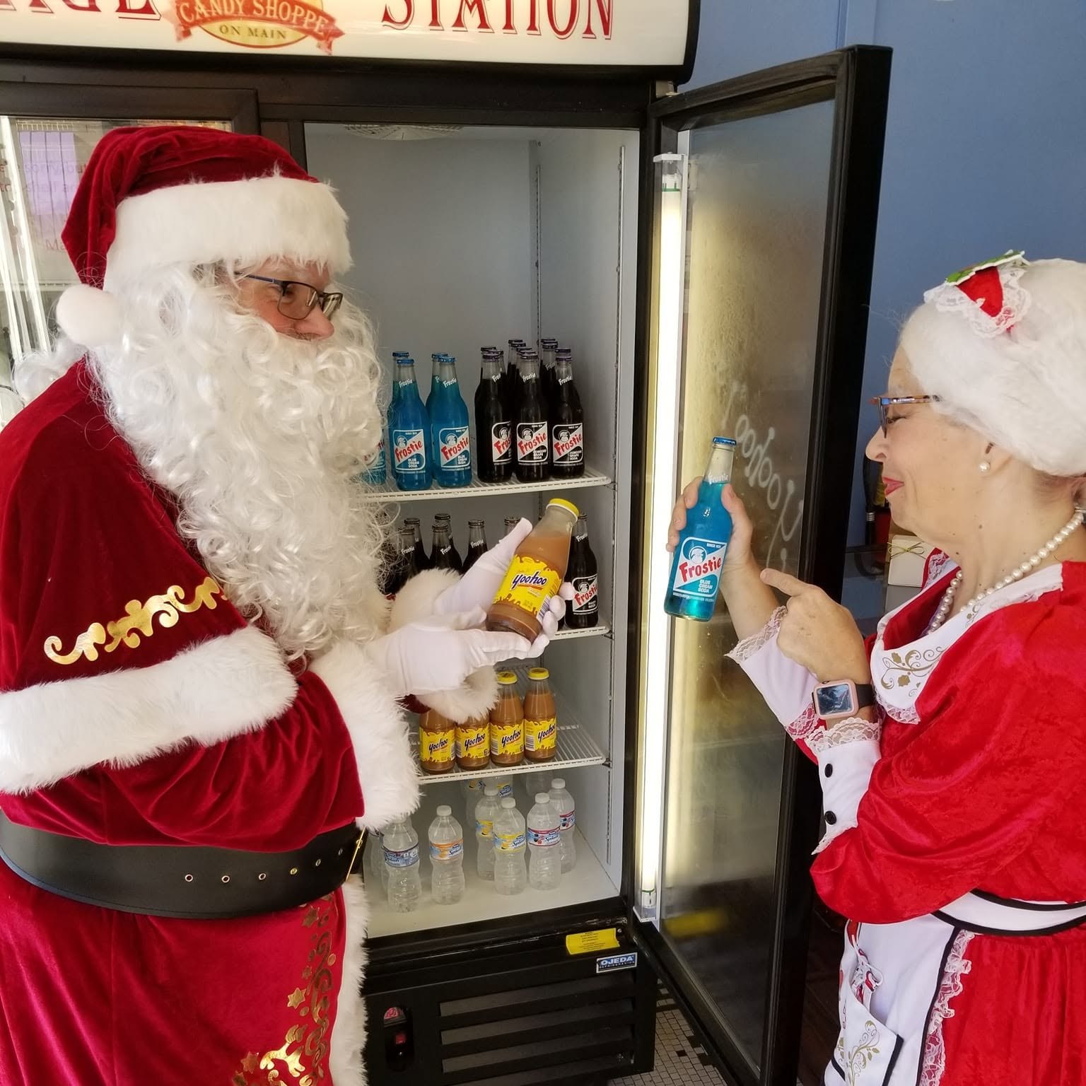 Santa and Mrs. Claus stocking the glass bottle cooler at The Candy Shoppe on Main